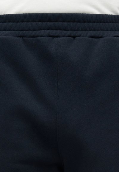 Μαύρη ελαστική ζώνη μέσης και πάνω τμήμα μαλακού υφάσματος παντελονιού, που δείχνει τη ραφή στο κέντρο μπροστά και τις λεπτομέρειες ραφής.