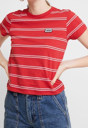 Kobieta w czerwono-białej pasiastym t-shircie Vans wsuniętym do wysokociętych niebieskich jeansów, ręce na biodrach.