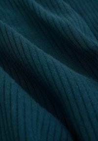 Tessuto a coste di un verde teal scuro con un aspetto morbido e testurizzato. Il materiale presenta linee verticali che creano un motivo ondulato in tutto il tessuto.