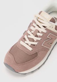 New Balance sneaker in soft pink and beige, featuring a textured suede and mesh upper, thick cream laces, and a grey rubber sole.