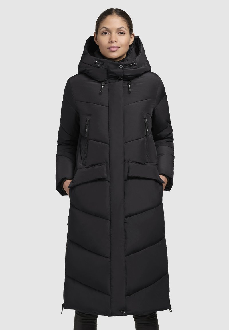 Lång svart puffjacka med huva, som har två framfickor med dragkedja och en klaffficka. Chevron-quiltad design; tillverkad av mjukt, vadderat tyg.
