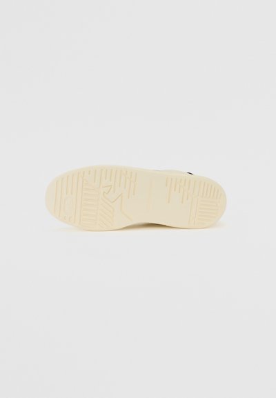Sneaker outsole featuring a smooth beige rubber material, textured with various grooves and patterns for enhanced grip and durability.