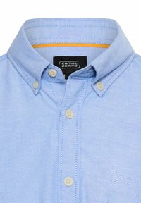 Light blue button-up shirt made of cotton. Features a standard collar, plastic buttons, and subtle stitched detailing. Camel Active logo on side.