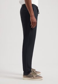 Marineblauwe joggers met elastische tailleband, met zijzakken, slim fit ontwerp, gladde textuur en trekkoord, gecombineerd met lichtgekleurde sneakers.