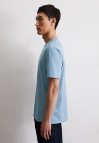 Short-sleeved, light blue t-shirt made of cotton, featuring a crew neckline and a relaxed fit, displayed on a model from the side.