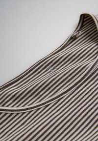 Gros plan sur un tissu rayé marron et blanc avec un col rond et une petite étiquette indiquant « THE SET » près du col.
