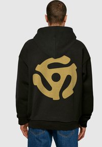 Sort hættebluse med et stort guld vinylplade logo på ryggen. Designet er oversized, med en blød stofstruktur og rummelig pasform.