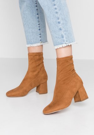 Bottines en daim marron à la coupe ajustée, bout pointu et talon bloc. Les bottines présentent des coutures discrètes et une tige souple.