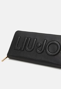 Cartera de cuero negro con el logo en relieve "LIU·JO", superficie texturizada y tirador de cremallera en color dorado.