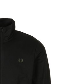 Zwarte jas met rits en hoge kraag, gemaakt van gladde stof. Heeft een subtiel groen logo op de borst, zonder zichtbare patronen of hardware.