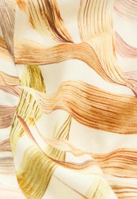Tissu avec des motifs fluides en forme de rubans dans des nuances d’orange, de jaune et de marron sur un fond crème, montrant la texture et des plis doux.