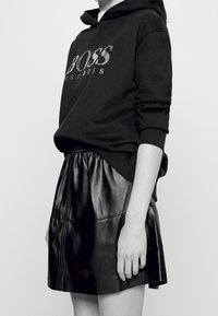 Sudadera negra con el logo "BOSS" en gris. Combinada con una falda plisada de cuero negro, que muestra una textura suave y una cintura elástica.
