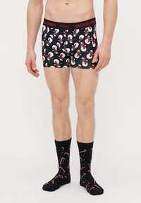 Μαύρα μπόξερ με στάμπα χιονάνθρωπου και κόκκινη μέση· σετ με μαύρες κάλτσες που έχουν σχέδια καραμελών και νιφάδων χιονιού.