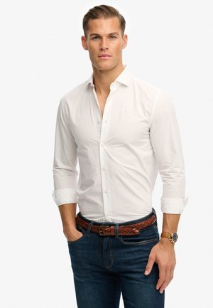 Witte overhemd met lange mouwen, slim fit, gemaakt van lichtgewicht stof. Gecombineerd met donkerblauwe jeans en een gevlochten bruine riem.