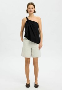 Svart topp med en axel, med draperad tygdetalj och vriden rem, i kombination med ljusgrå knälånga shorts. Svarta vävda ballerinas kompletterar outfiten.