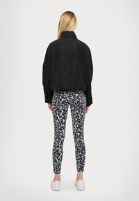 Veste noire courte sur des leggings gris à pois léopard noirs. Des baskets blanches complètent la tenue. Tissu lisse et design ajusté.