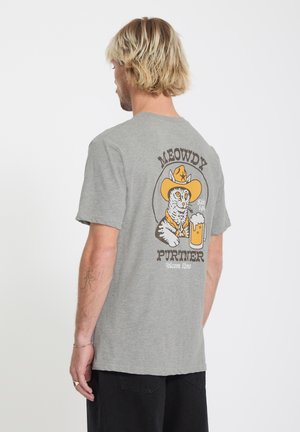 Uomo biondo di spalle che indossa una maglietta grigia con l'immagine di un gatto con cappello da cowboy che tiene una boccale di birra e la scritta "Meowdy Purtner" sul retro.