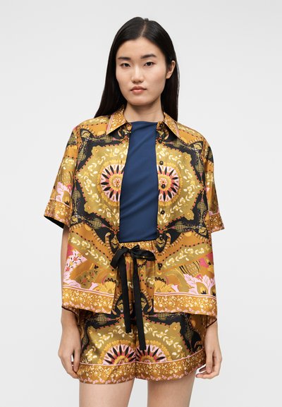 Camisa de manga corta estampada en dorado, negro y rosa; cuenta con un ajuste relajado y cierre de botones. Combina con pantalones cortos a juego, anudados a la cintura.