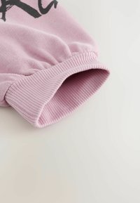 Fondo della manica di un pullover rosa chiaro realizzato in tessuto morbido con texture a coste, caratterizzato da un orlo elasticizzato per una vestibilità aderente.