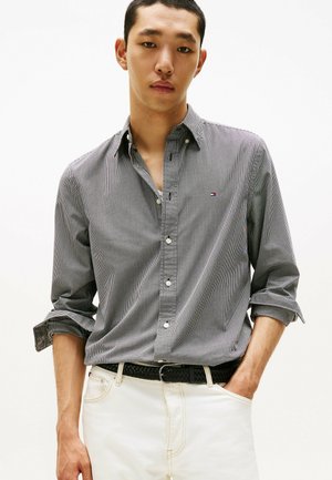 Chemise à manches longues à rayures grises et blanches avec un col, arborant un petit logo sur la poitrine gauche, assortie à un pantalon blanc.