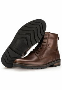 Botas de tobillo de cuero marrón con superficie texturizada, puntera redonda, cordones en la parte delantera y una suela de goma con un patrón en zigzag.