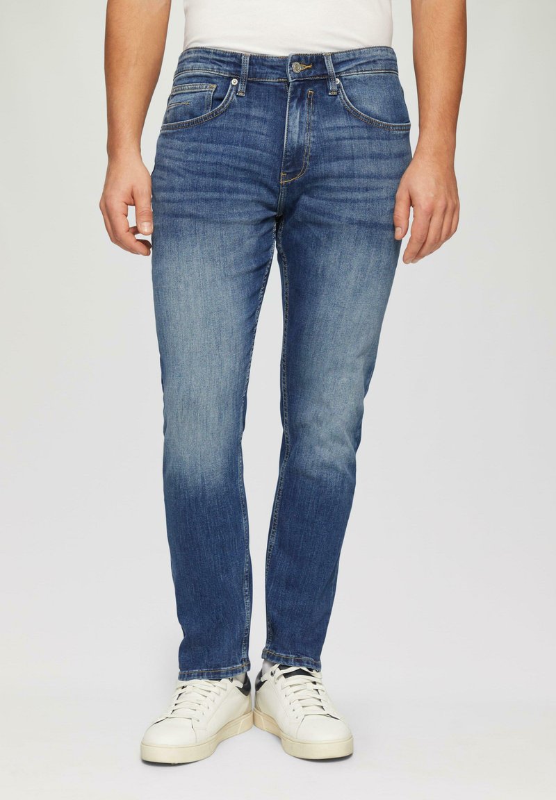 Blauwe denim jeans met een slim fit, lichte vervaging op de dijen, vijf zakken en een rits, gecombineerd met witte sneakers.