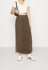 Falda maxi de estampado de leopardo en marrón con material transparente, con un dobladillo con volantes. Combinada con una camiseta corta blanca y zapatillas blancas.