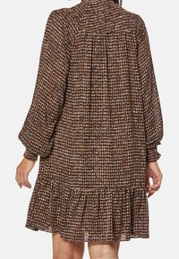 Braun gemustertes Kleid mit rüschigem Saum, gerafftem Ausschnitt und voluminösen Ärmeln. Das Material wirkt leicht und hat eine texturierte Oberfläche.