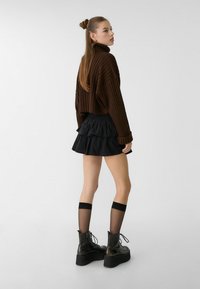 Brun ribbad polotröja, svart flerradig volangkjol, knähöga svarta strumpor och kraftiga svarta snörboots. Släta texturer genom hela outfiten.
