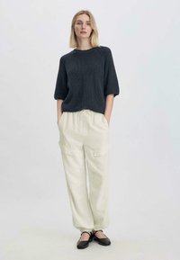 Neulettu tummanharmaa teksturoitu paita, jossa on lyhyet ja leveät hihat, yhdistettynä kermavärisiin, väljiin cargo-housuihin, joissa on sivutaskut. Mustat kengät.