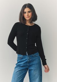 Black long-sleeve cardigan featuring a round neckline and button closures down the front, paired with blue high-waisted jeans.