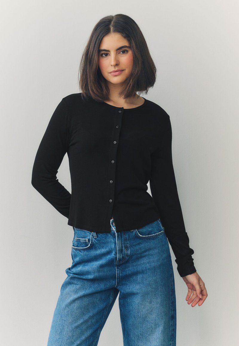 Black long-sleeve cardigan featuring a round neckline and button closures down the front, paired with blue high-waisted jeans.