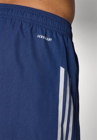 Mørkeblå træningsshorts med elastisk talje, prydet med hvide lodrette striber og "AEROREADY" logo på siden. Glat struktur.