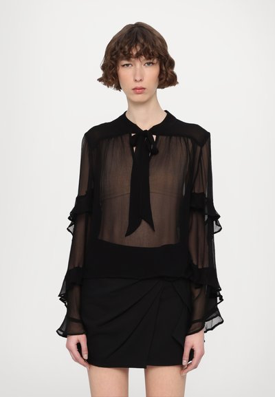 Black, sheer blouse with a tie neck, featuring ruffled sleeves, layered fabric, and a solid color at the hem. Paired with a black skirt.