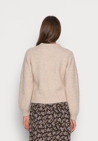 Maglione lavorato a maglia color crema con una vestibilità comoda, superficie testurizzata, orlo a costine e scollo rotondo, abbinato a una gonna con stampa floreale.