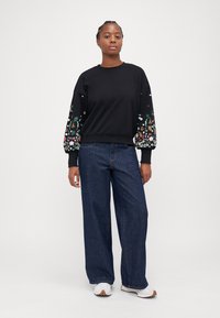 Melna džemperis ar izšūtām ziedu piedurknēm, plata džinsu bikses un baltas kedas. Puloverim ir ribota apkakle un piedurknes.