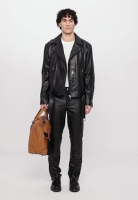 Zwarte leren motorjack met zilveren ritsen, gecombineerd met zwarte leren broek. Bruine leren tas, gedragen met zwarte laarzen.