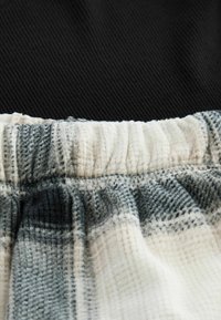Bomuldsblandingsstof med et struktureret ternet mønster i grå og off-white. Har en elastisk talje og en blød, let krøllet finish.