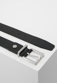Cintura in pelle nera con fibbia quadrata in argento, cinque fori di regolazione e una finitura opaca liscia. Presenta un design semplice con accenti minimi.