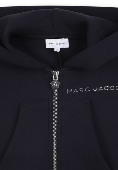 Felpa blu navy con zip completa, tasche frontali e zip con tirante a forma di fiore in argento. "MARC JACOBS" in lettere argento sul petto. Tessuto morbido.