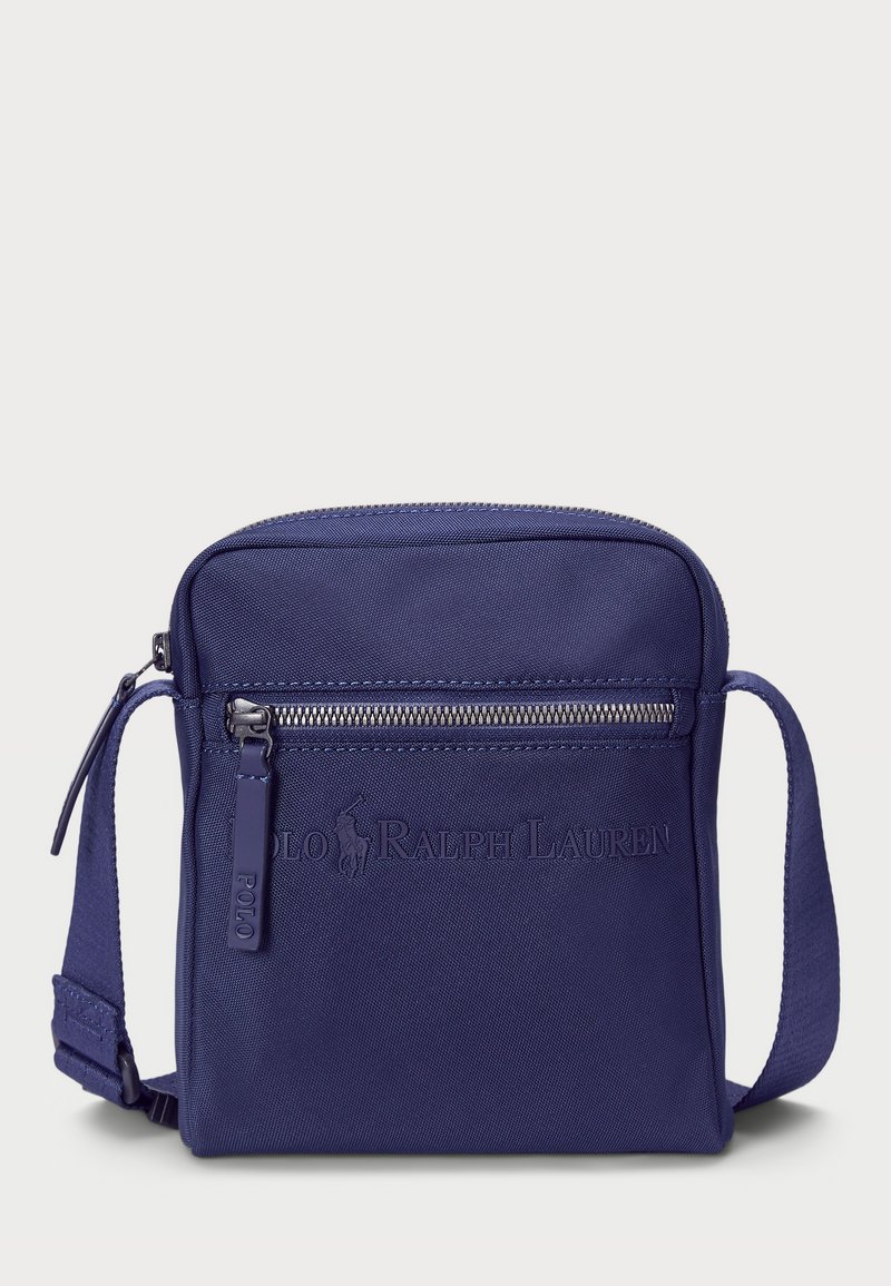 Geantă crossbody bleu închis, fabricată din nailon durabil, având un buzunar frontal cu fermoar, logo embosat și o curea plată ajustabilă.