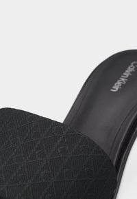 Μαύρο σανδάλι με λουράκι με υφή και διακοσμητικό μοτίβο και λείο πάτο με το λογότυπο της Calvin Klein.