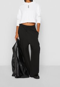 Bílá zkrácená mikina na zip s tkaničkou, doplněná volnými černými kalhotami s bočními kapsami. Přehazovaná černá kožená bunda.