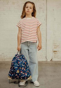 Gestreepte rood-witte shirt, lichtblauwe jeans en een trekkoordtas met een bloemenpatroon. Witte sneakers en natuurlijk textuur haar.