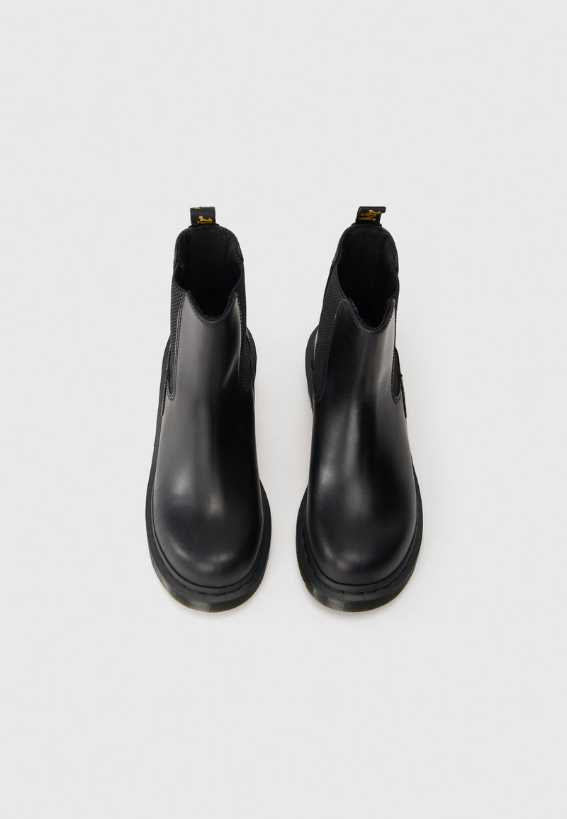 Par de botines de cuero negro con paneles laterales elásticos y tiradores sobre un fondo blanco.