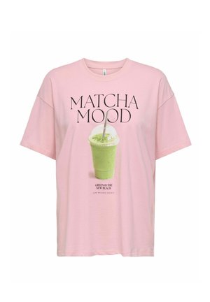 Jasnoróżowy t-shirt z napisem „MATCHA MOOD” nad zielonym napojem matcha w plastikowym kubku oraz „GREEN IS THE NEW BLACK” poniżej.