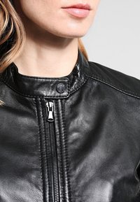 Svart läderjacka med ståkrage, framdragkedja och subtila sömnadsdetaljer. Slät textur, minimal hårdvaruaccents.