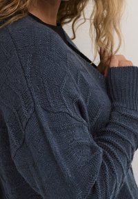 Cardigan lavorato a maglia di colore blu scuro con un motivo a rombi, caratterizzato da polsini a coste e un taglio rilassato, realizzato in un morbido materiale testurizzato.