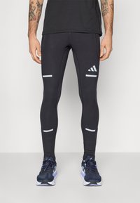 Leggings de sport noirs avec des accents réfléchissants. Présente un design ajusté, un tissu extensible et un logo sur la jambe gauche inférieure.