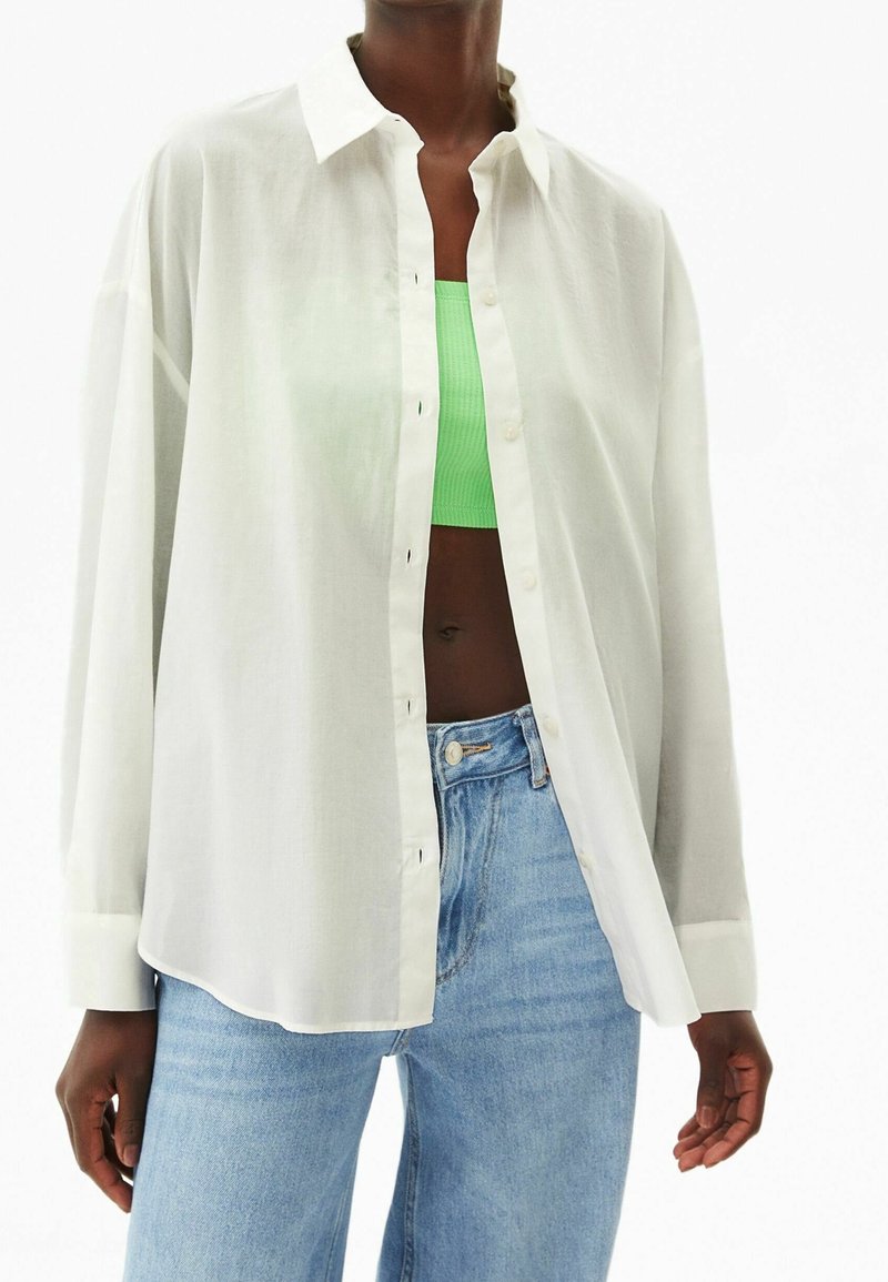White button-up shirt in lightweight fabric, relaxed fit, featuring long sleeves and a point collar, layered over a green crop top.